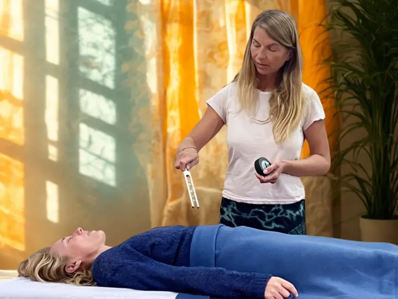 En una habitación luminosa y tranquila, un terapeuta sostiene un diapasón sobre una persona