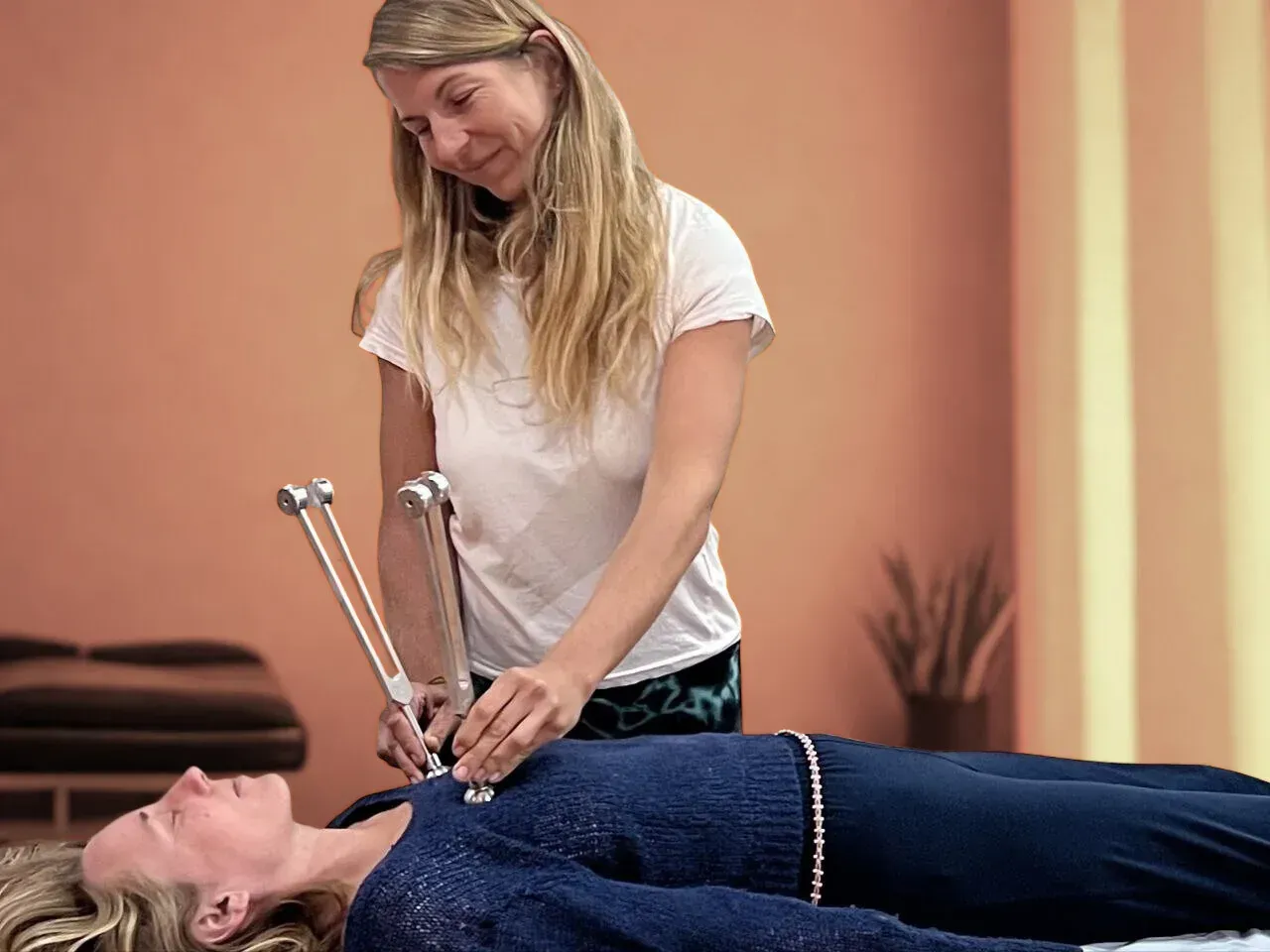 Un terapeuta sostiene dos diapasones sobre el pecho de una persona que está tumbada para una sesión de sonoterapia.