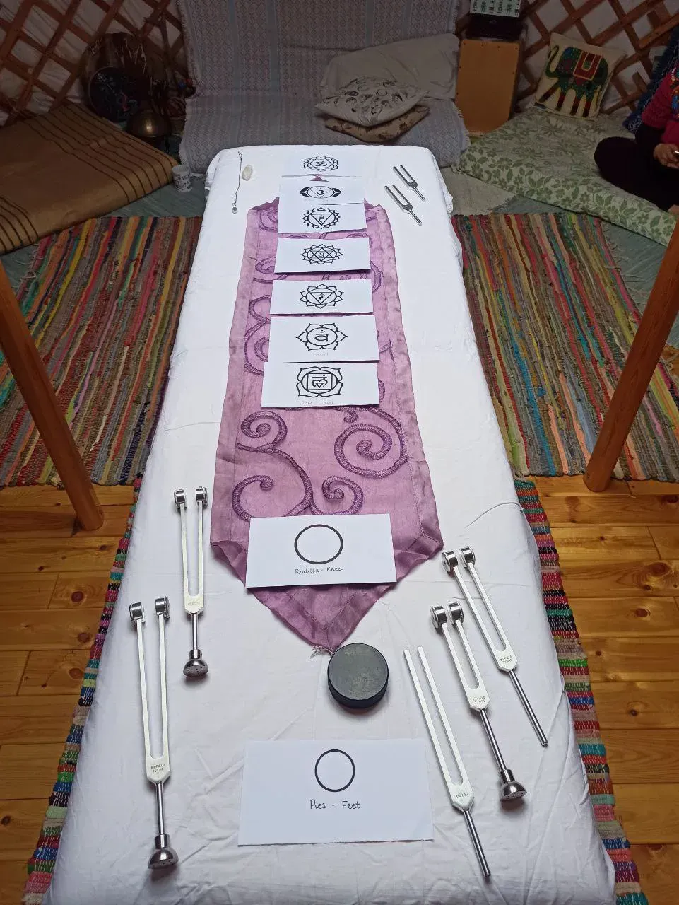 Una camilla de terapia cuenta con siete tarjetas con símbolos de chakras dispuestas sobre un tapete morado