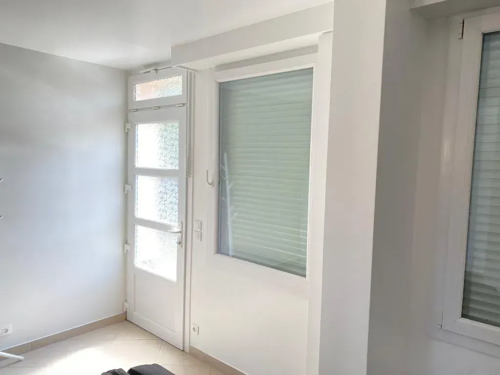 Façade intérieure avec une porte vitrée et deux fenêtres équipées de volets roulants