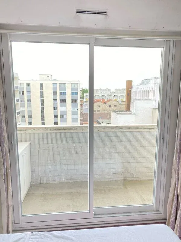 Baie vitrée blanche donnant sur un balcon d'immeuble classique