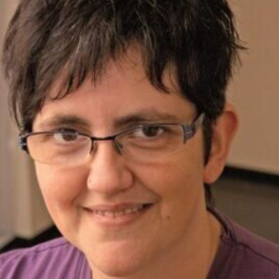 Eine Frau mit Brille und lila Hemd lächelt in die Kamera.