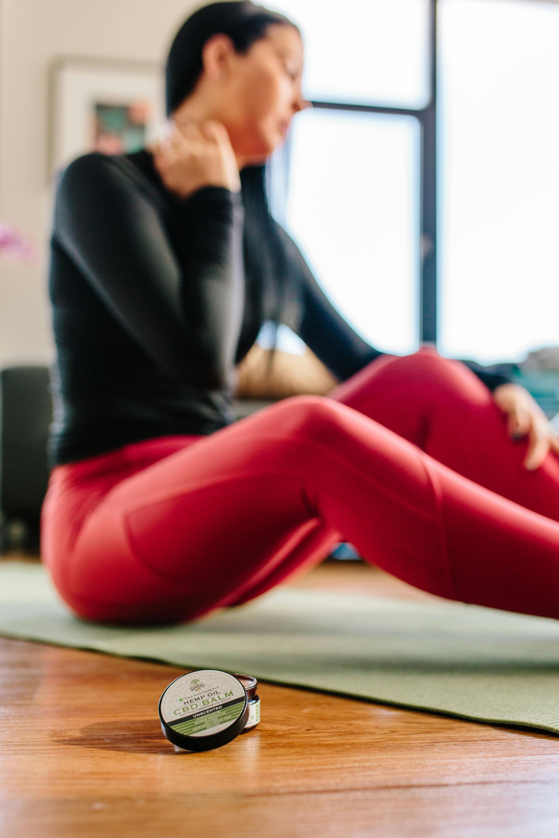 Eine Frau sitzt auf einer Yogamatte und auf dem Boden liegt eine Uhr.