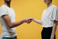 Ein Mann und eine Frau geben sich vor gelbem Hintergrund die Hand.