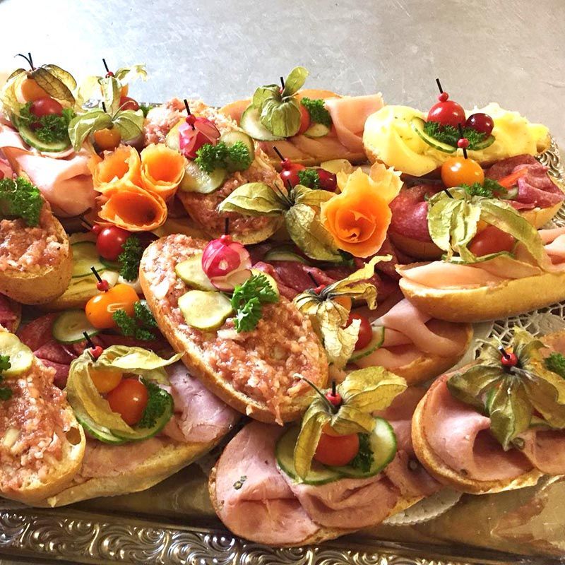 Eine Platte mit belegten Brötchen, dekoriert mit Blumen, Tomaten und Schinken.