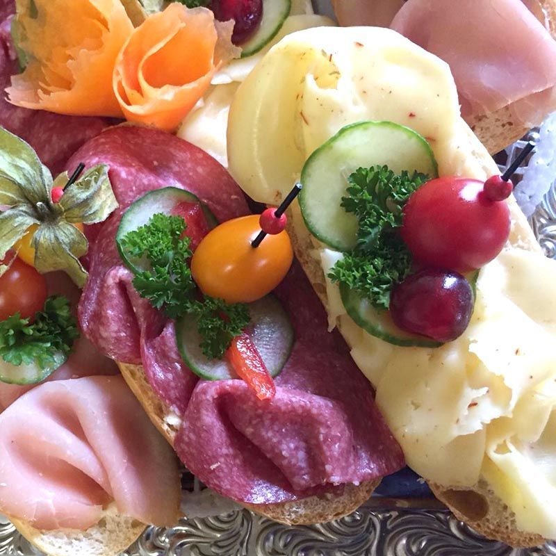 Nahaufnahme einer Platte mit belegten Brötchen, belegt mit Fleisch, Käse, Gemüse und Beilagen.