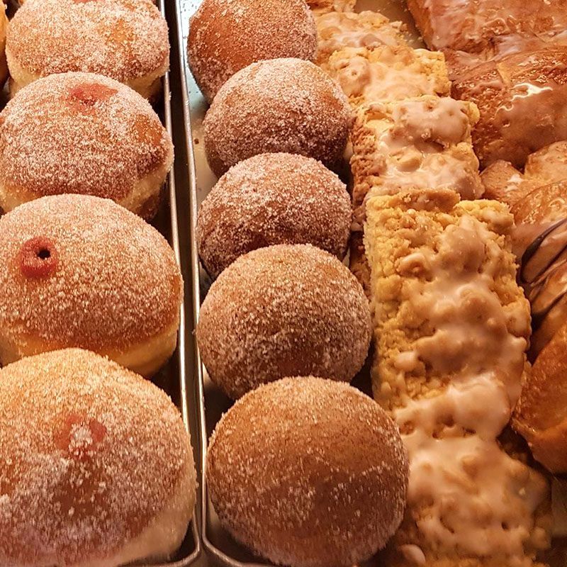 Nahaufnahme eines Tabletts mit verschiedenen Donuts: mit Zucker überzogen, gefüllt und glasiert, ausgestellt.