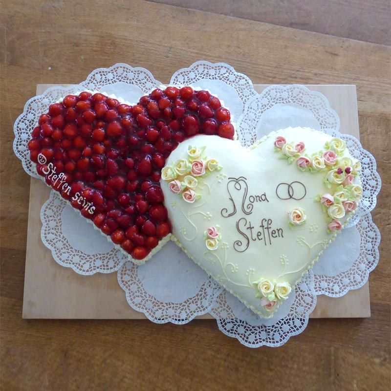 Herzförmige Hochzeitstorte mit Erdbeeren und Zuckerguss, verziert mit Namen und Ringen.