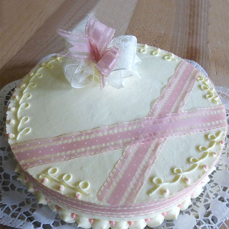 Runder Kuchen, verziert mit hellgelbem Zuckerguss, einem rosa Schleifenkreuz und einer Schleife.