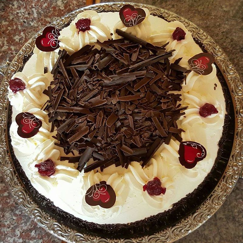Schwarzwälder Kirschtorte, rund, mit Schlagsahne, Schokoraspeln, Herzbonbons und Kirschen, auf einem Silbertablett.