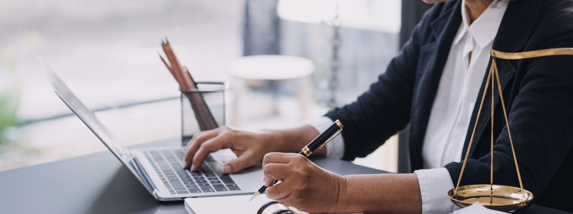 Personne travaillant sur un ordinateur portable, en train d'écrire, avec une balance de la justice sur son bureau ; intérieur.