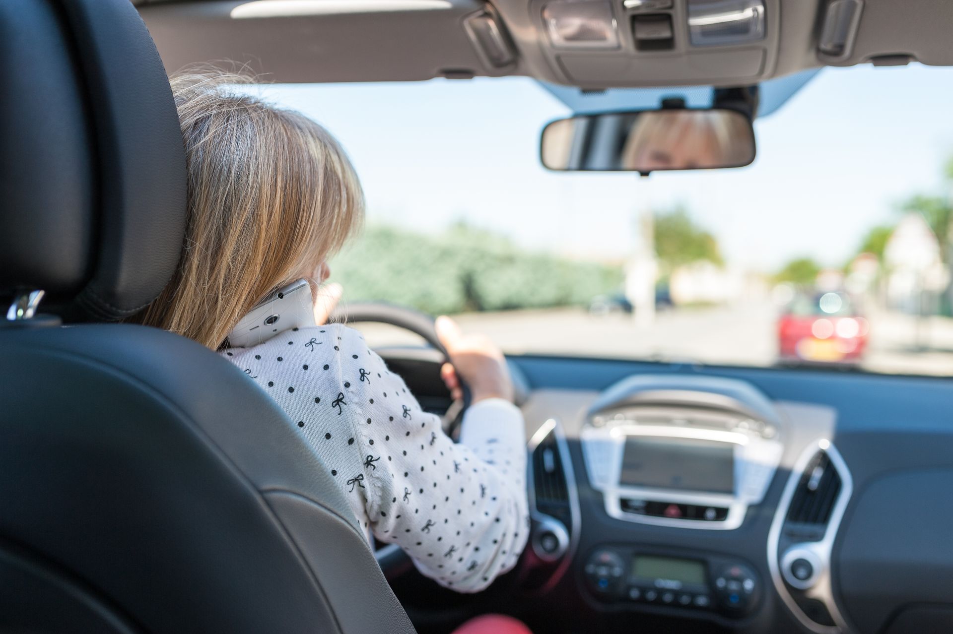 Personne conduisant une voiture, mains sur le volant, vue depuis la banquette arrière.