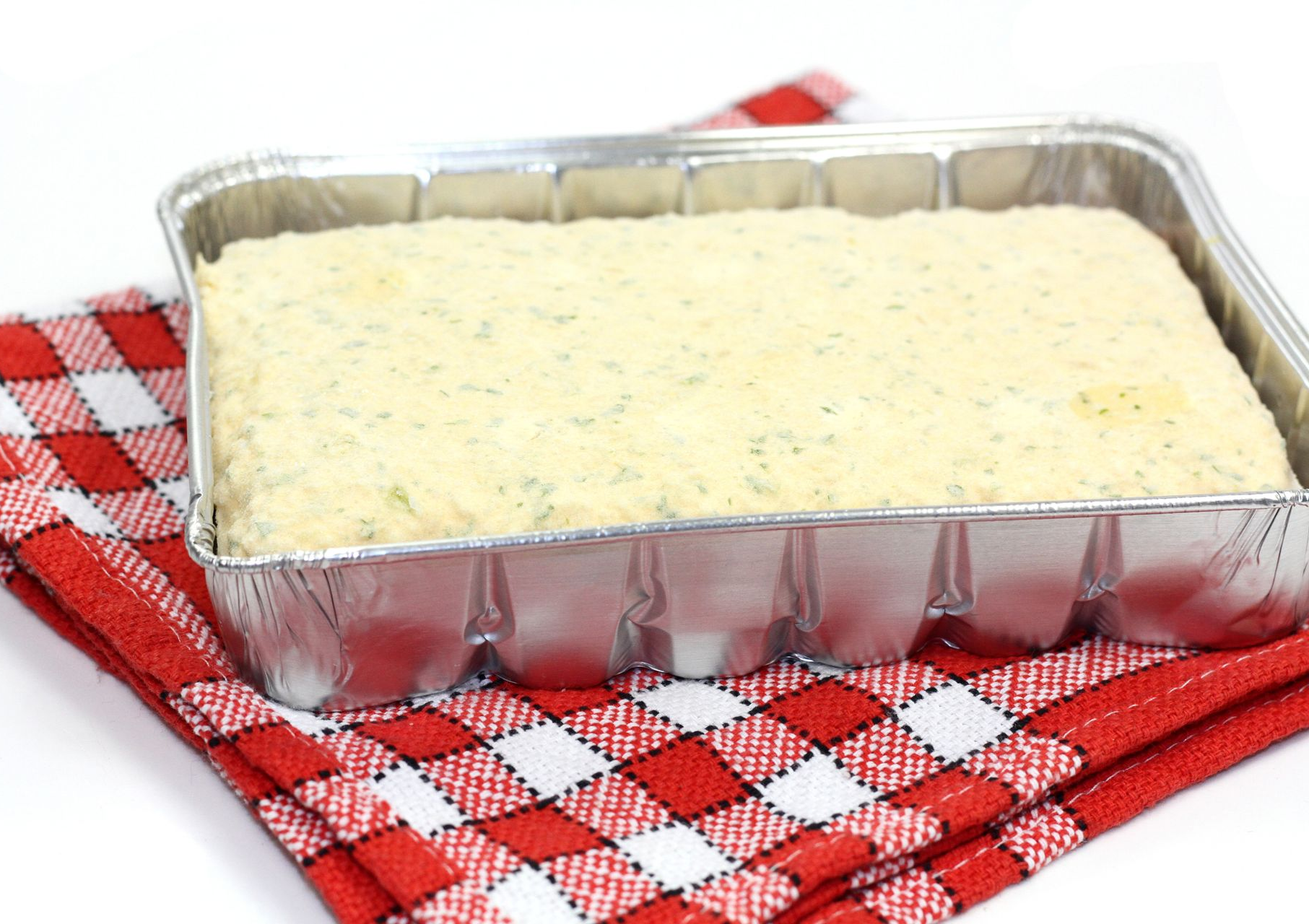 Plat en aluminium rempli de gratin crémeux, posé sur une nappe à carreaux.