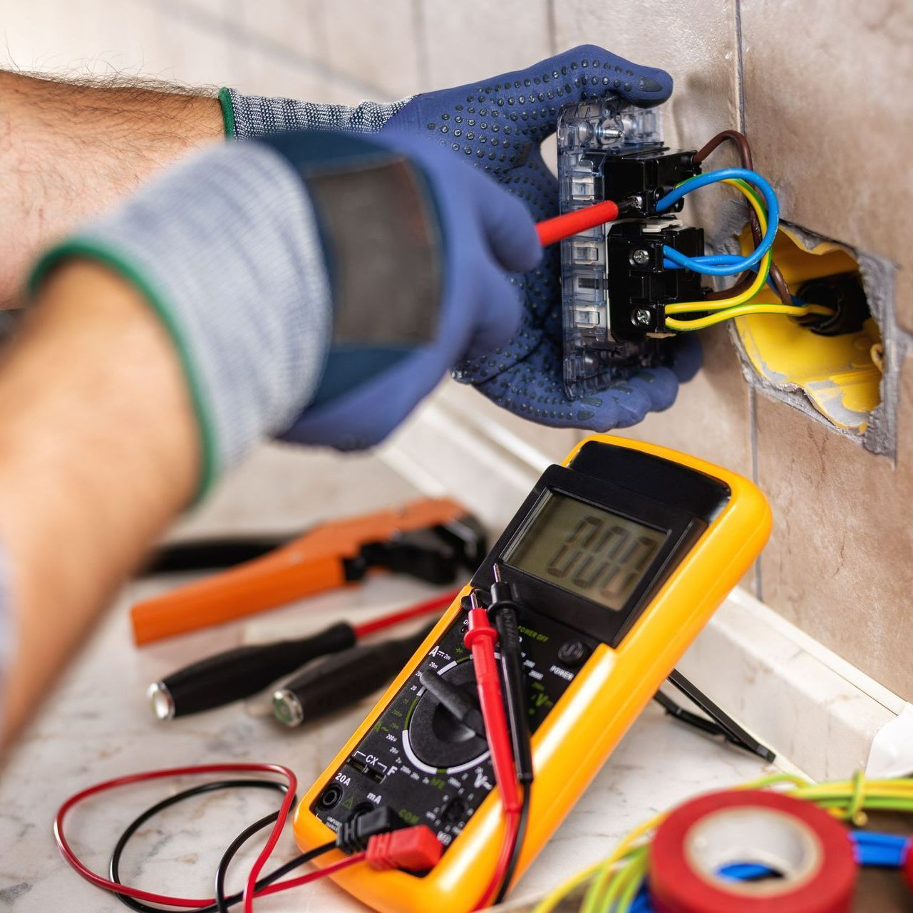 Électricien avec des gants qui contrôle une prise électrique murale