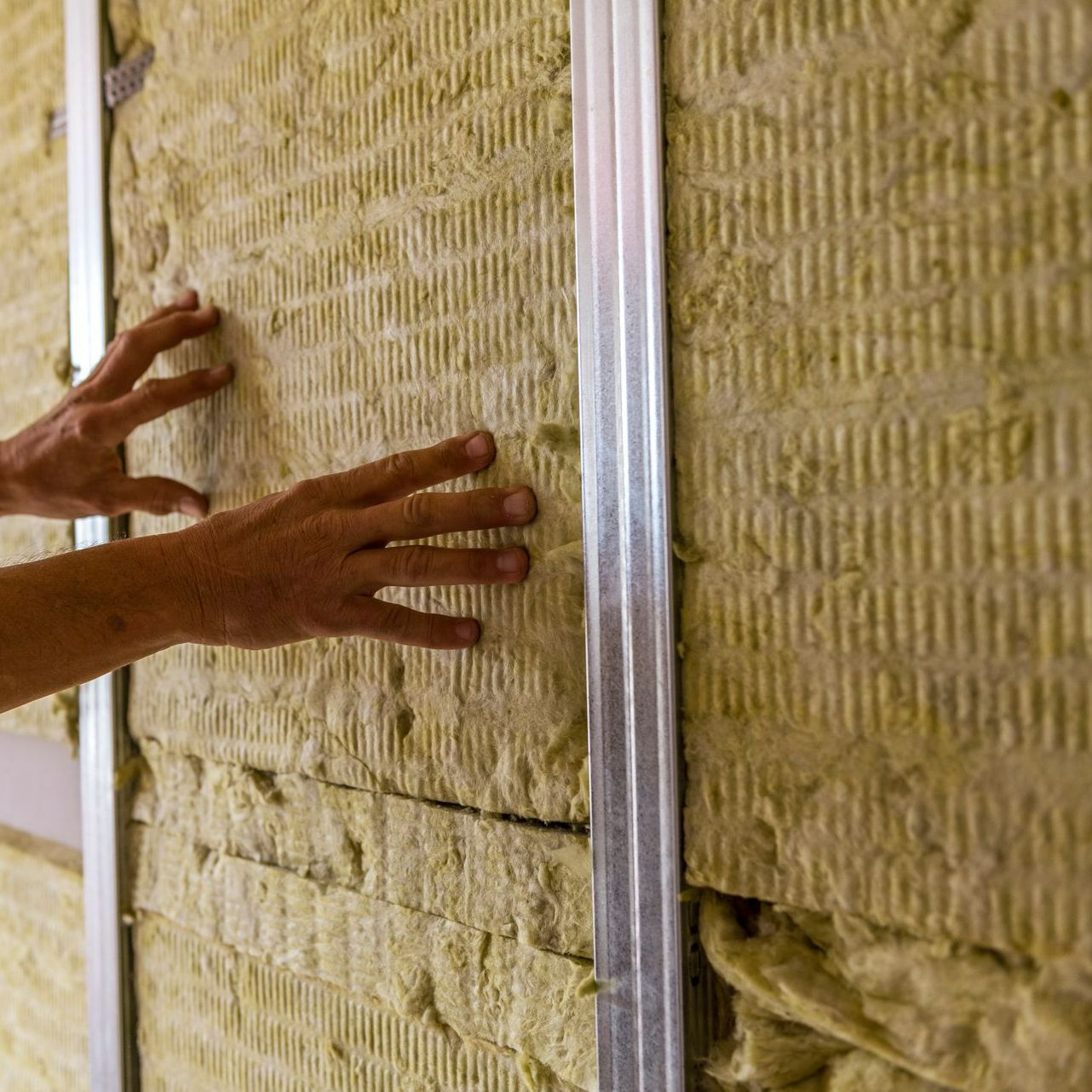 Deux mains posant un isolant sur des cloisons