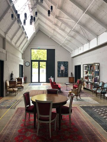 Salle d'exposition avec haut plafond blanc, tapis rouge, table ronde, chaises et bibliothèques près de grandes fenêtres