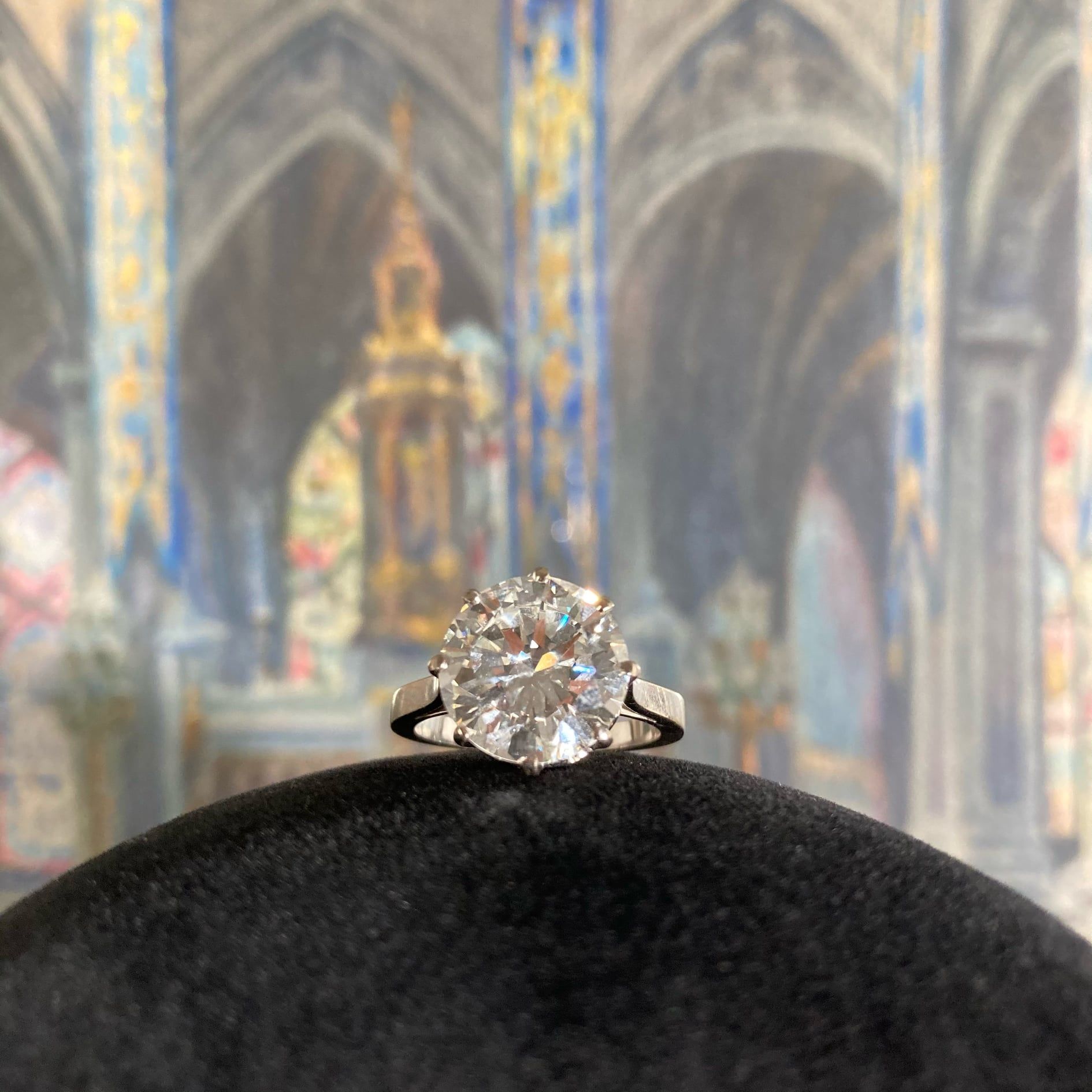 Bague en diamant présentée sur un écrin de velours noir avec un fond flou évoquant une cathédrale.