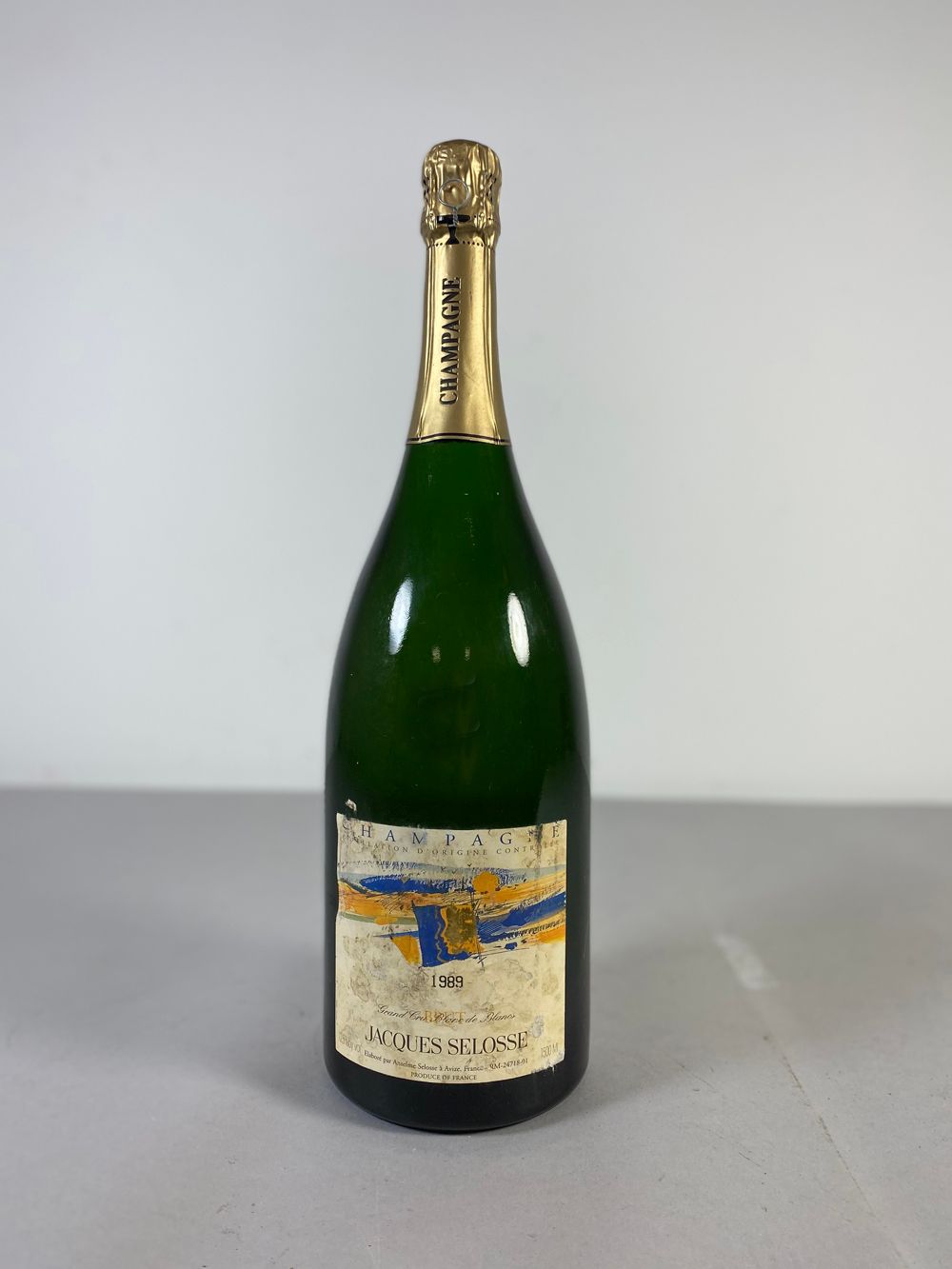 Bouteille de champagne verte avec étiquette crème et feuille d'or sur fond gris.