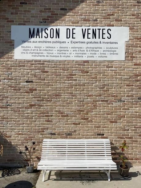 Banc blanc contre un mur de briques sous une enseigne Maison de Ventes.