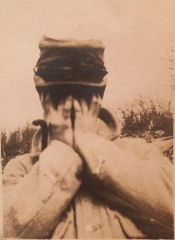 Une personne portant un chapeau de soldat se couvre le visage avec les deux mains.