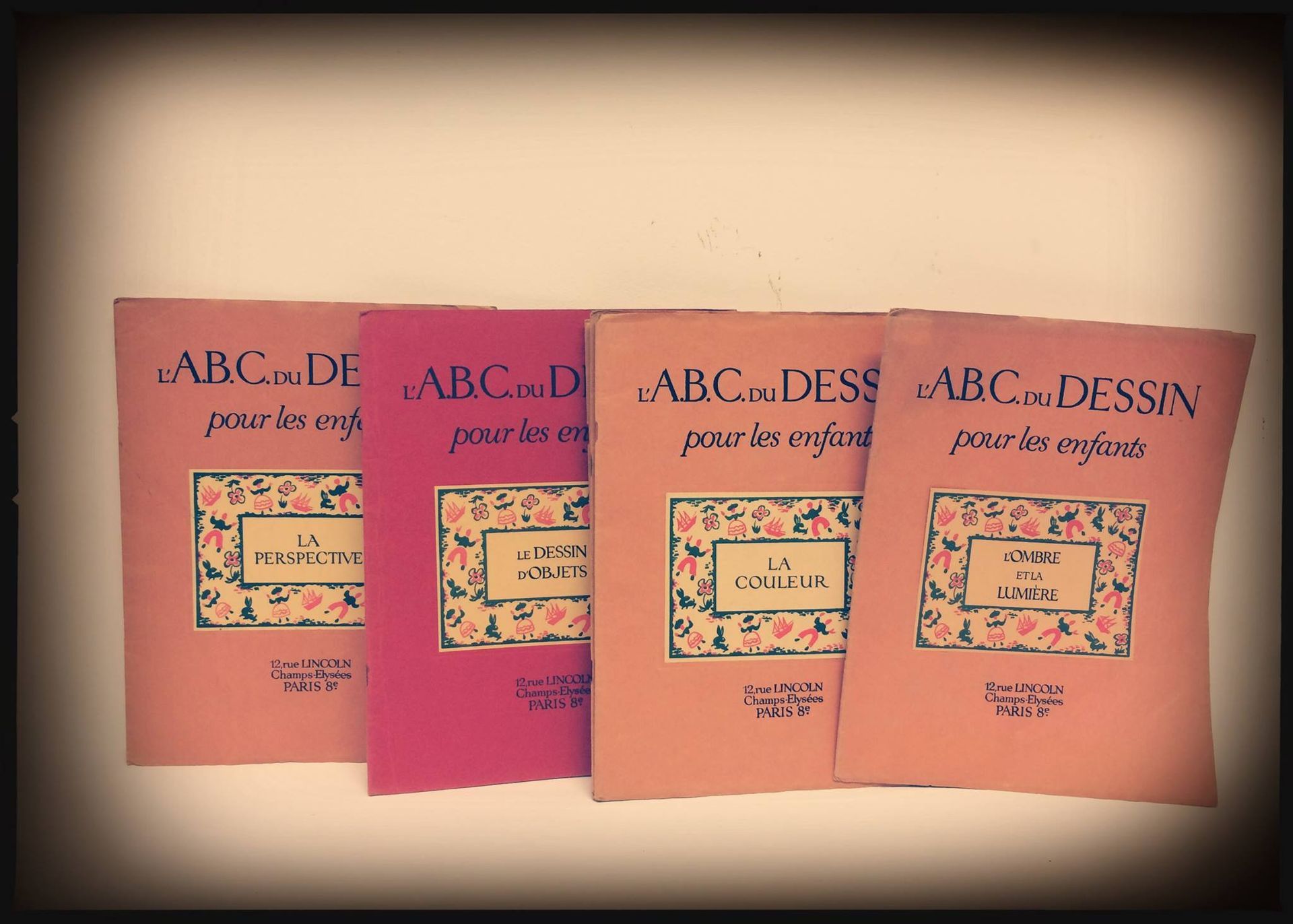 Quatre livres pour enfants français ABCD aux couleurs pastel, disposés en rangée sur un fond beige.