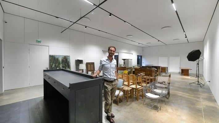 Un pianiste assis à un piano à queue dans une salle remplie d'œuvres d'art, avec des tapis et des tableaux ornementaux.
