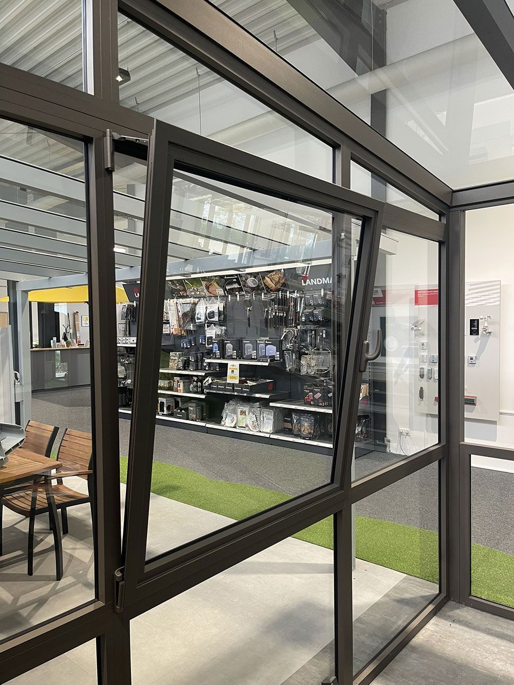 Offenes Fenster in der Glaswand eines Gebäudes; brauner Rahmen, Gegenstände aus dem Innenraum ausgestellt.