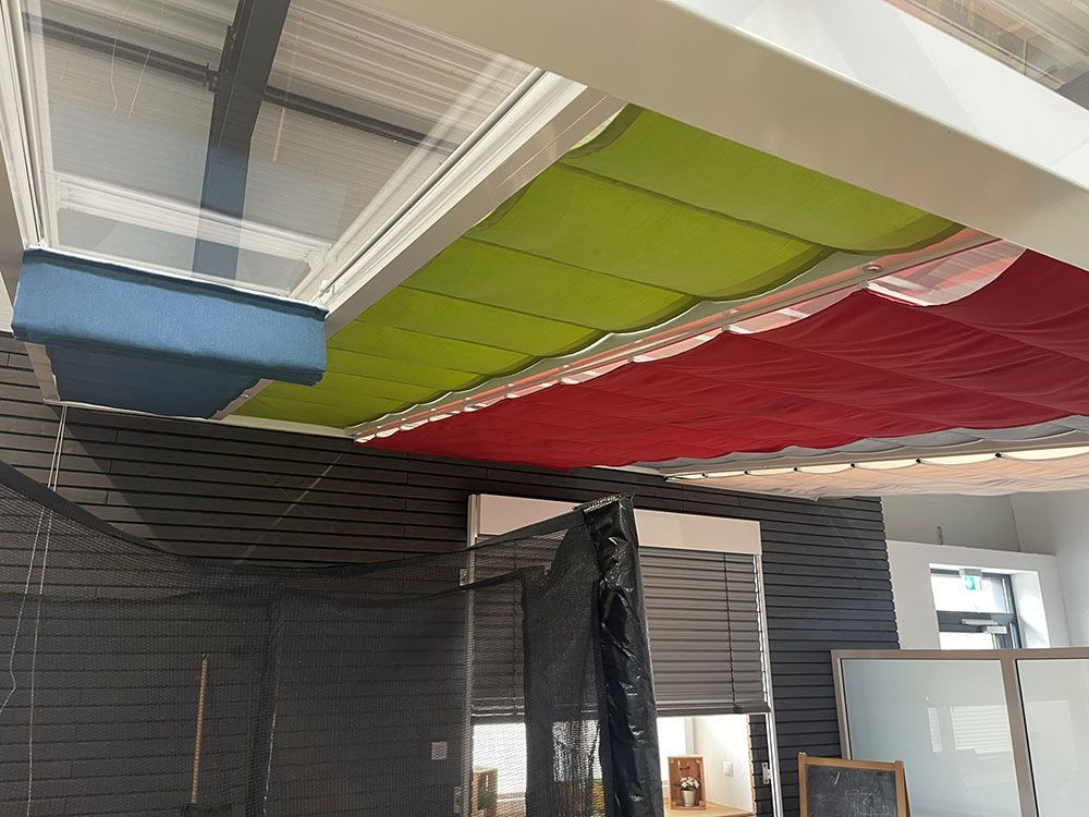 Mehrfarbige Markisenpaneele in Blau, Grün und Rot, die unter einer weißen Decke angebracht sind.