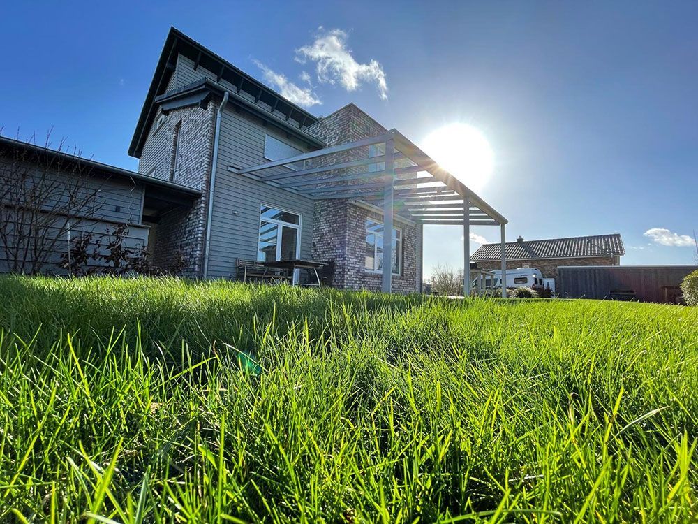 Grünes Gras vor einem Haus an einem sonnigen Tag. Die Sonne scheint hell.