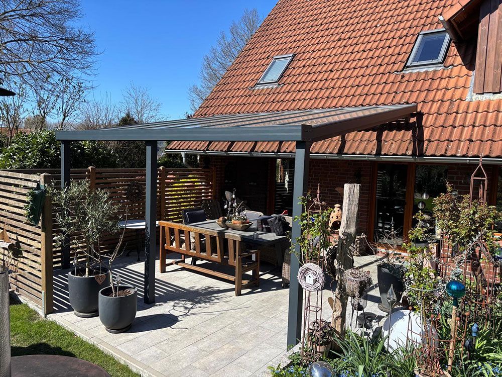 Terrasse mit Pergola, gedecktem Esstisch und umlaufendem Garten vor einem Backsteinhaus.