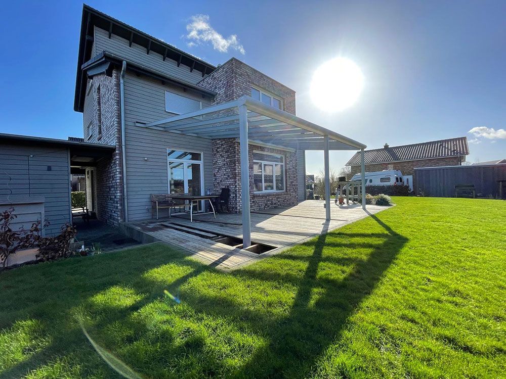 Haus mit Terrasse und Pergola an einem sonnigen Tag. Grünes Gras umgibt das Gebäude.