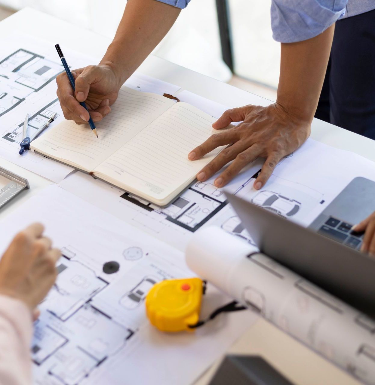 Ein Mann schreibt in ein Notizbuch, während ein anderer Mann einen Laptop benutzt.