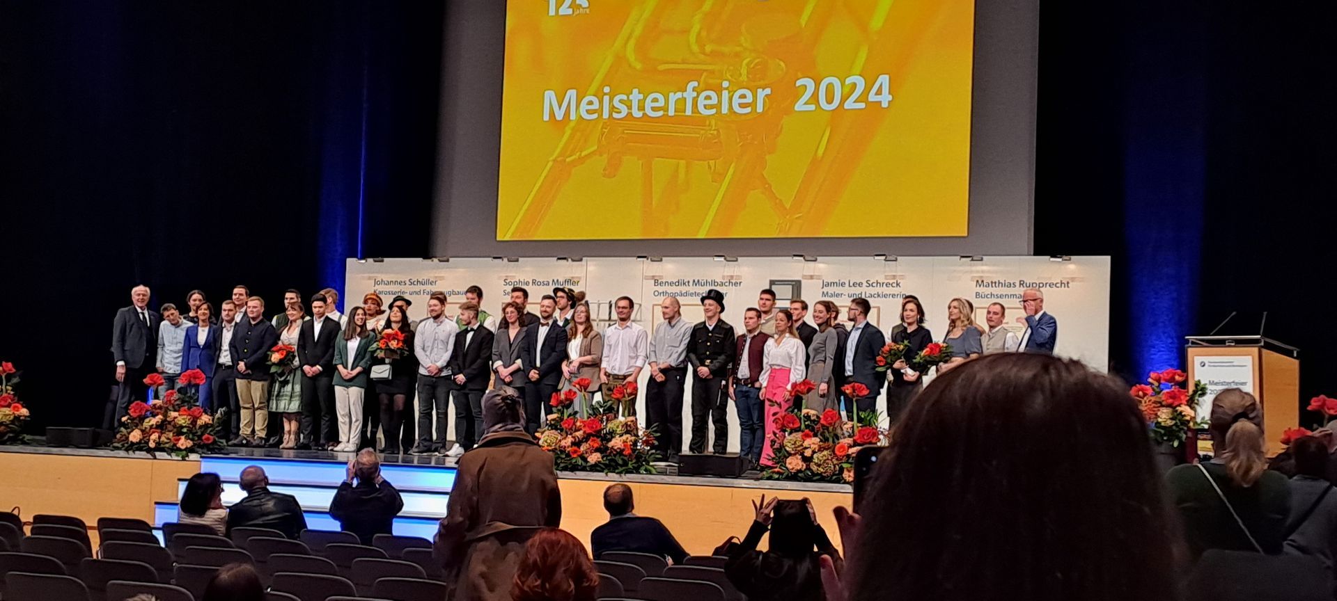 Feierliche Bühne mit „Meisterfeier 2024“ und Gruppe von Absolventen.