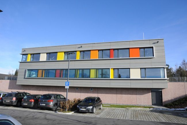 Moderne Gebäudefassade mit farbigen Fassadenelementen und großzügigen Fensterflächen.