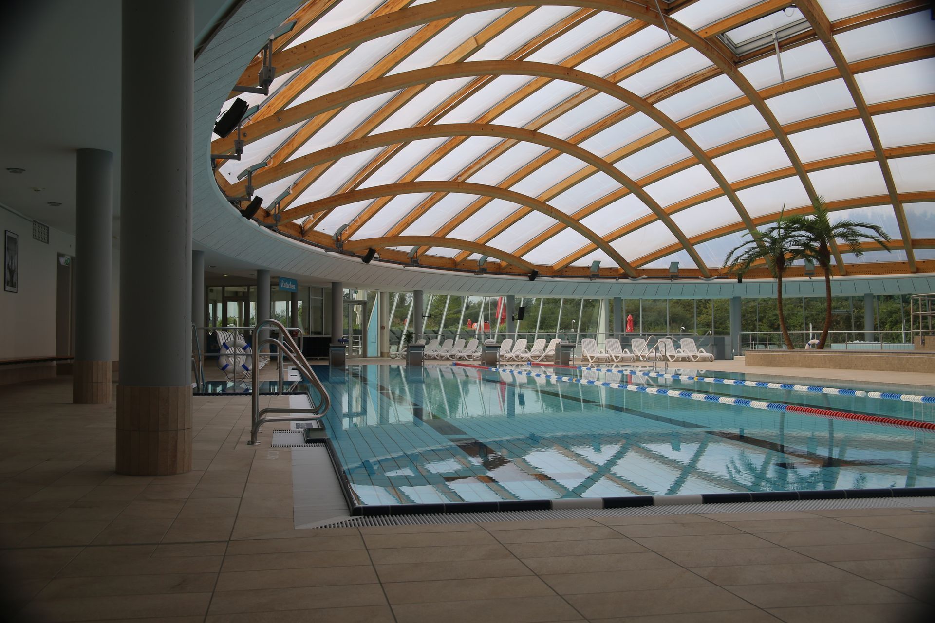 Schwimmbecken im Thermenbad unter einer großzügigen Holzdachkonstruktion mit weitläufigem Innenraum.