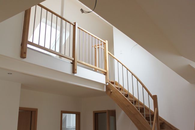 Heller Innenraum mit Holztreppe, Galerie und Holzgeländer in moderner Wohnarchitektur.