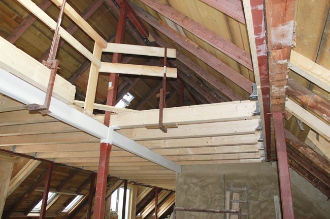 Offene Dachkonstruktion aus Holz und Metall mit sichtbaren Balken, Trägern und teilweise fertigem Innenausbau.