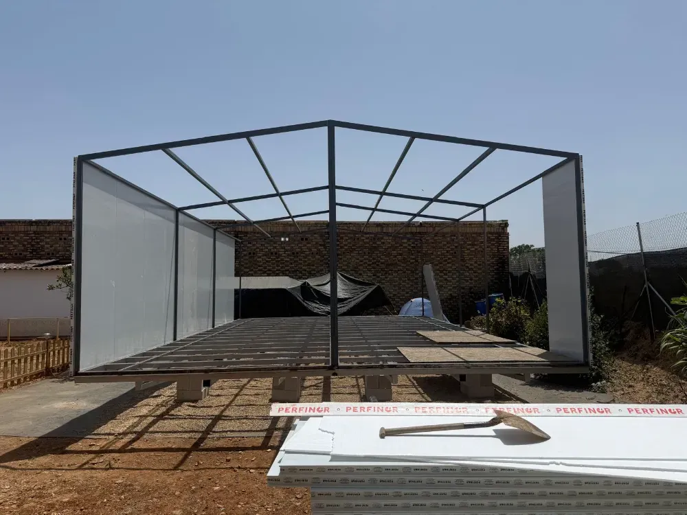 Estructura de marco de metal con paneles blancos en construcción, entorno exterior soleado.