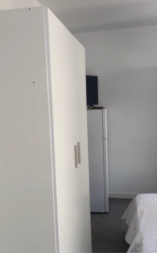 Armario blanco en un dormitorio minimalista con una cama y un pequeño televisor en la esquina.