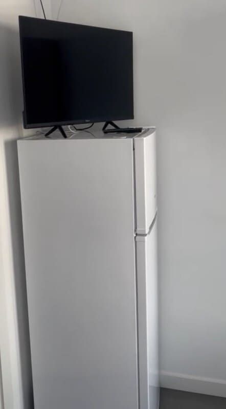 Un televisor negro encima de un refrigerador blanco en una habitación sencilla.