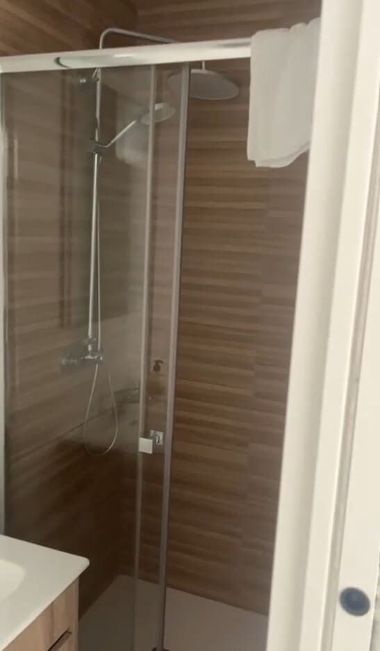 Baño moderno con ducha, mampara de cristal y azulejos de pared con aspecto de madera.