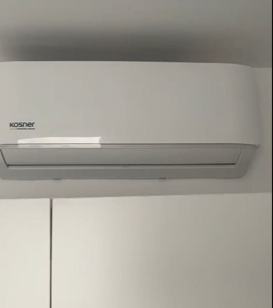 Aire acondicionado blanco montado en la pared, encima de un armario o ropero blanco.
