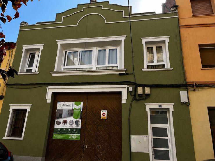 Fachada de edificio de color verde oliva con ventanas con marcos blancos y una gran puerta marrón, vista desde la calle.