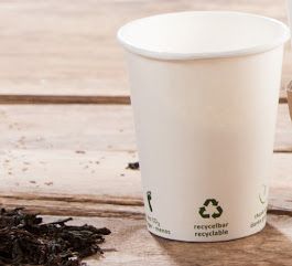Un vaso de papel está sobre una mesa de madera al lado de un montón de tierra.