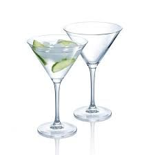 Dos copas de martini con una rodaja de pepino en ellas sobre un fondo blanco.