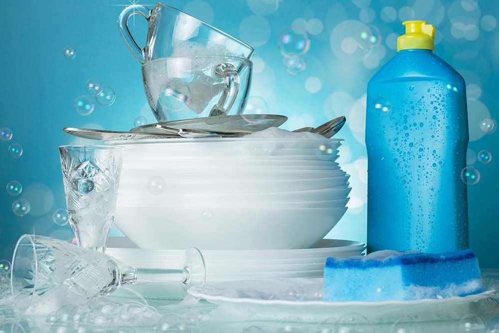 Platos, jabón y esponja con espuma. Botella azul de jabón lavavajillas, con burbujas sobre un fondo azul claro.