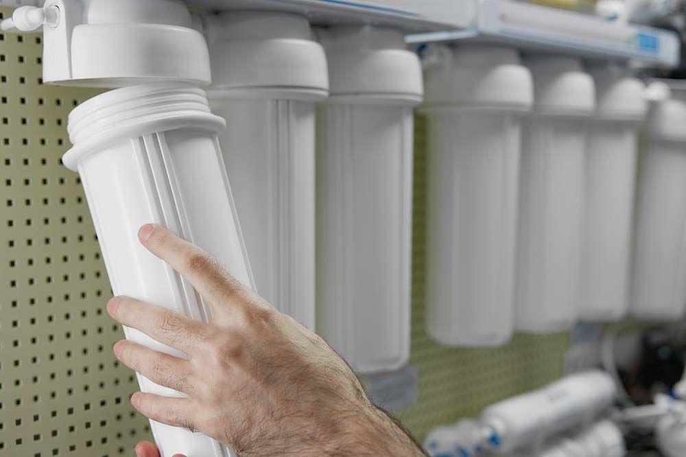 Mano sosteniendo un filtro de agua blanca, reemplazando uno en una fila de filtros, probablemente para un sistema de purificación de agua.