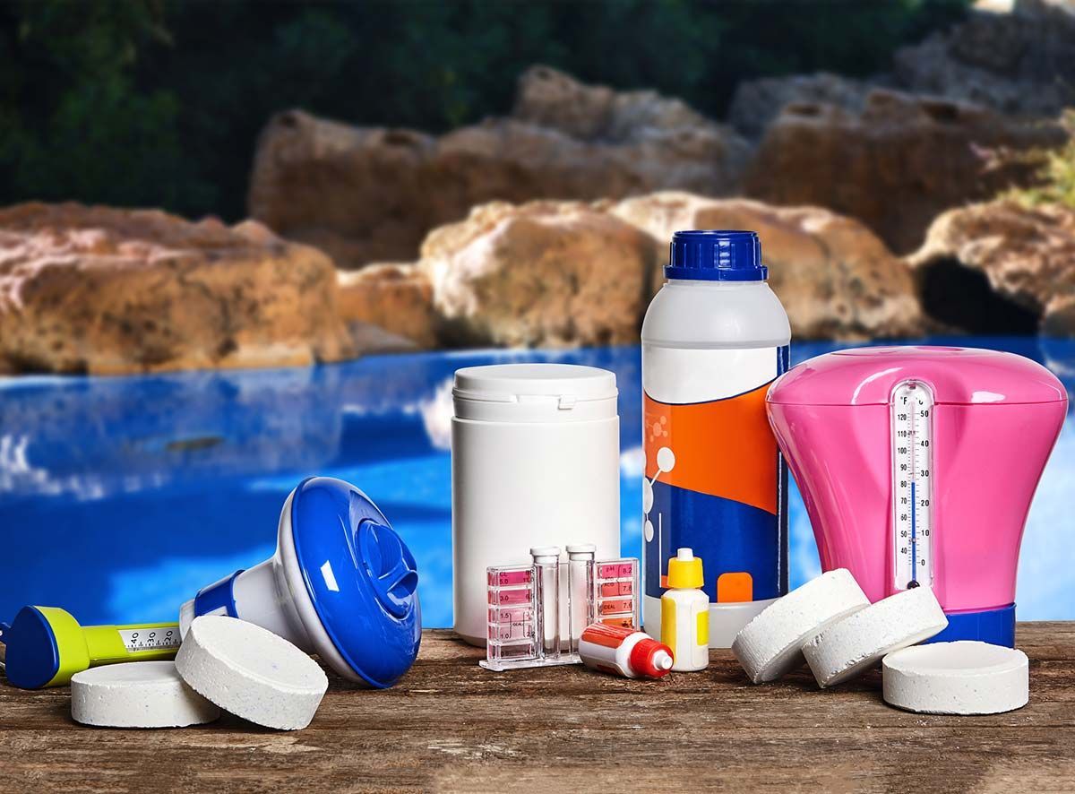 Productos químicos y suministros para piscinas sobre una superficie de madera cerca de una piscina.