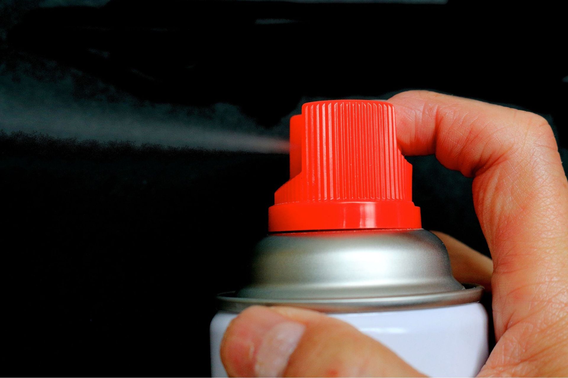 Una persona está rociando una lata de pintura en aerosol con una tapa roja.