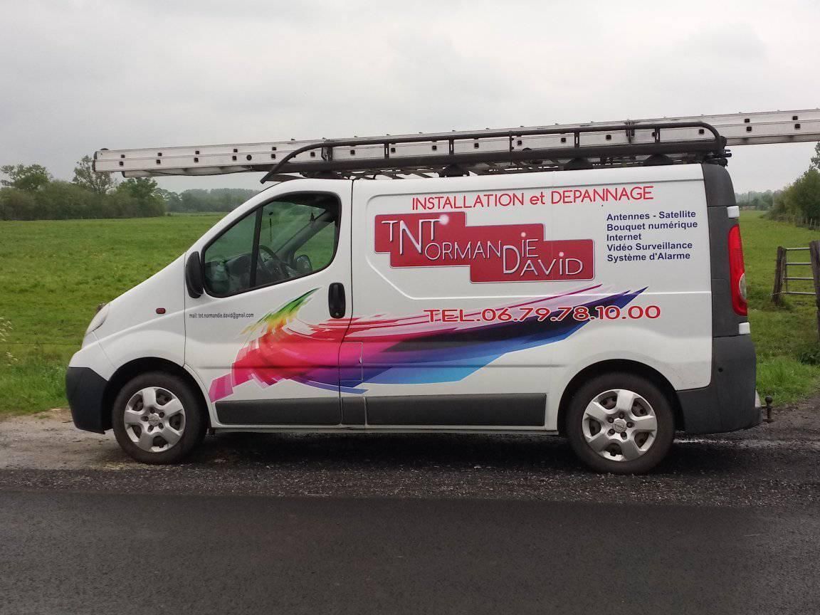 Fourgonnette blanche avec une échelle sur le toit, portant l'inscription TNT Normandie David.